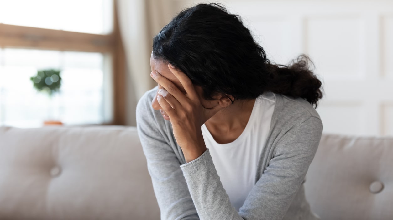 A woman sitting on a couch with her hands on her head.