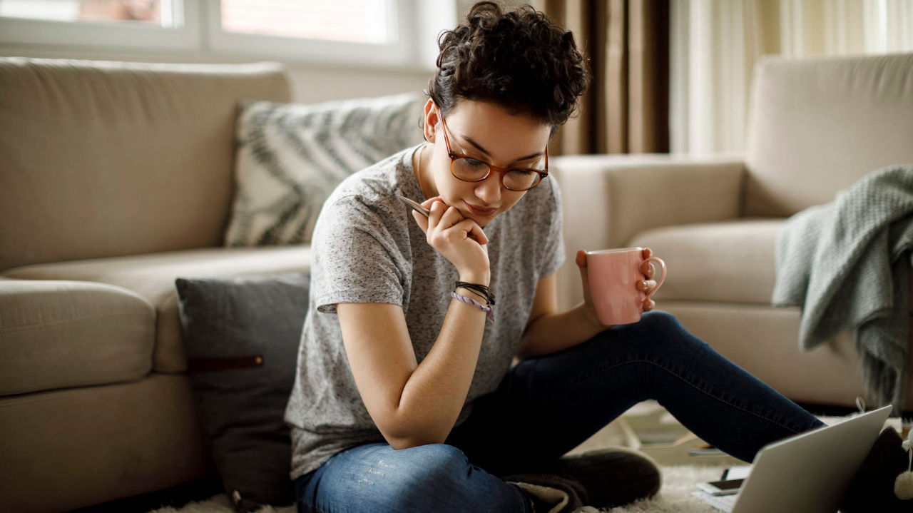 A woman sitting on the floor with a laptop and papers.