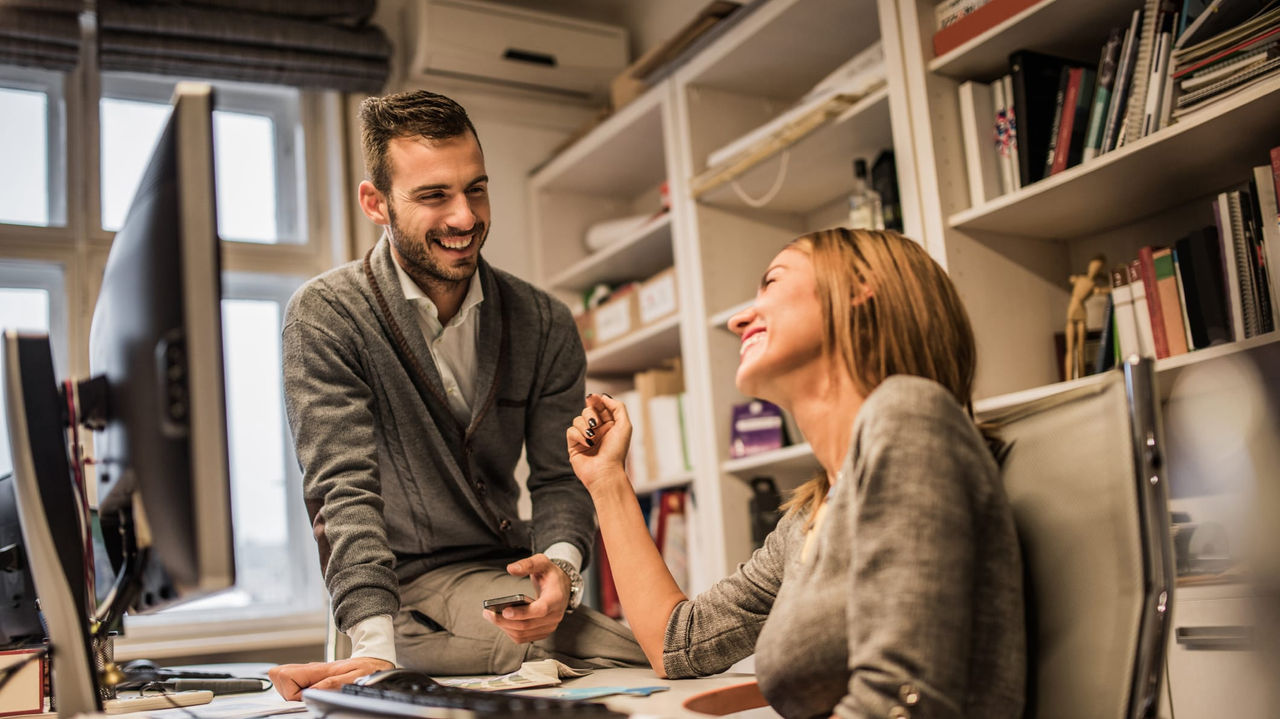 A man and woman are sitting at a desk in an office.