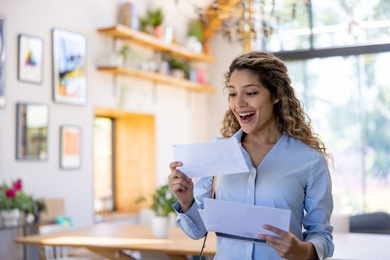 Excited woman at home reading good news in a letter in the mail - domestic life concepts