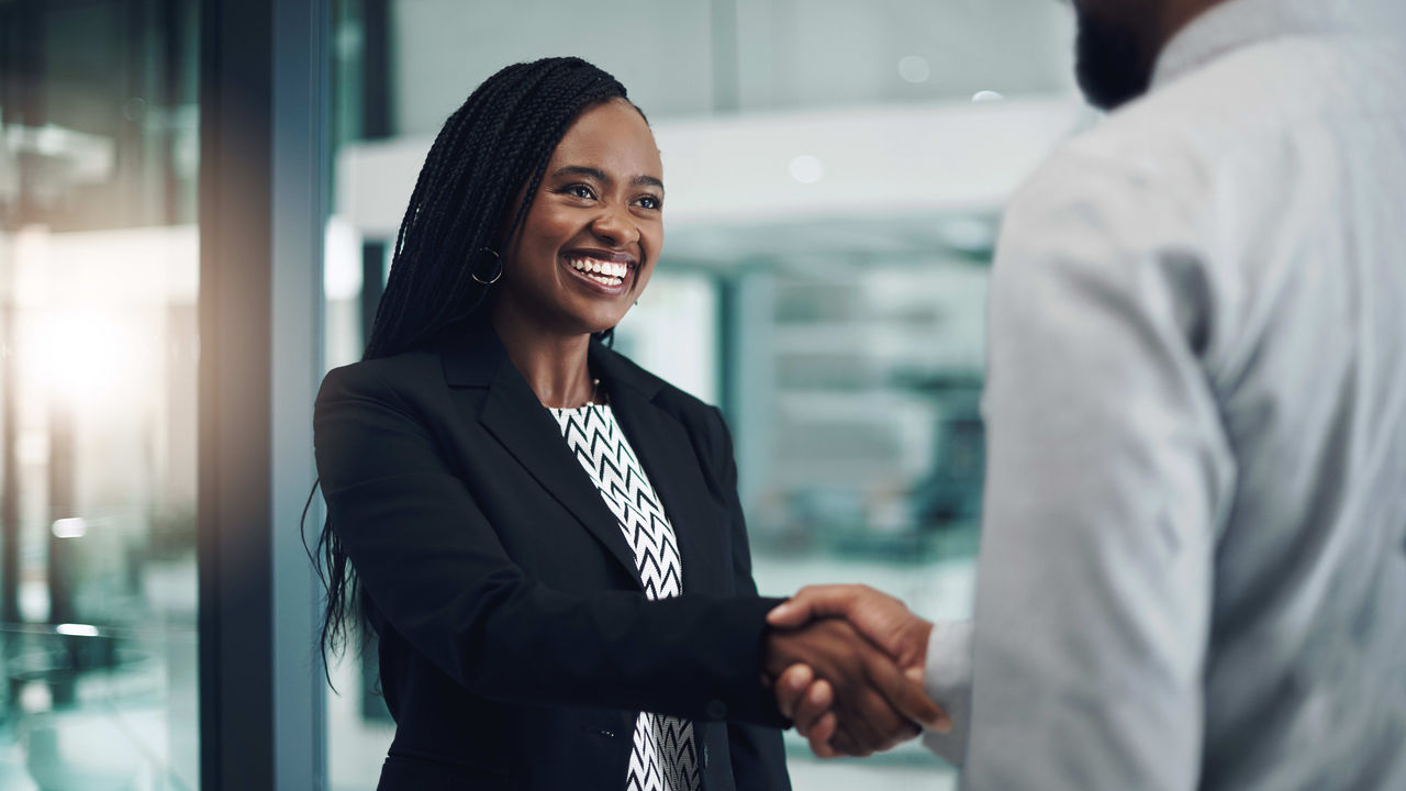 A business woman shakes hands with a man in an office.