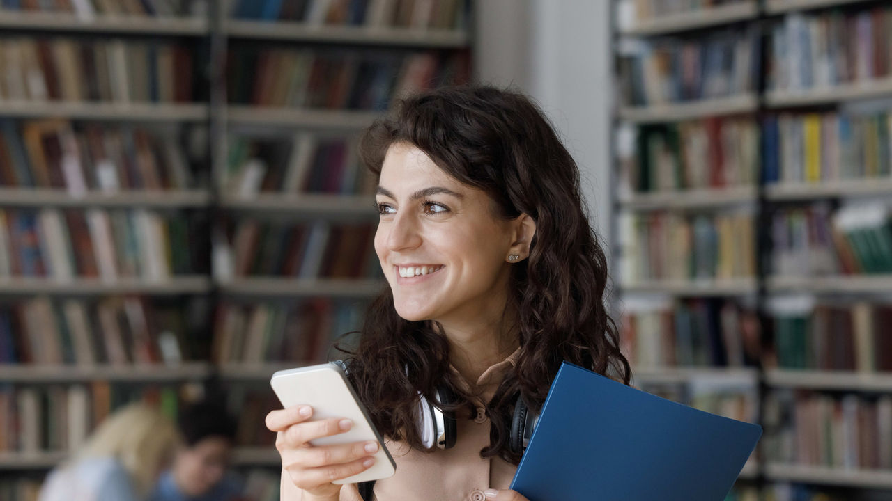 A woman holding a cell phone in a library.