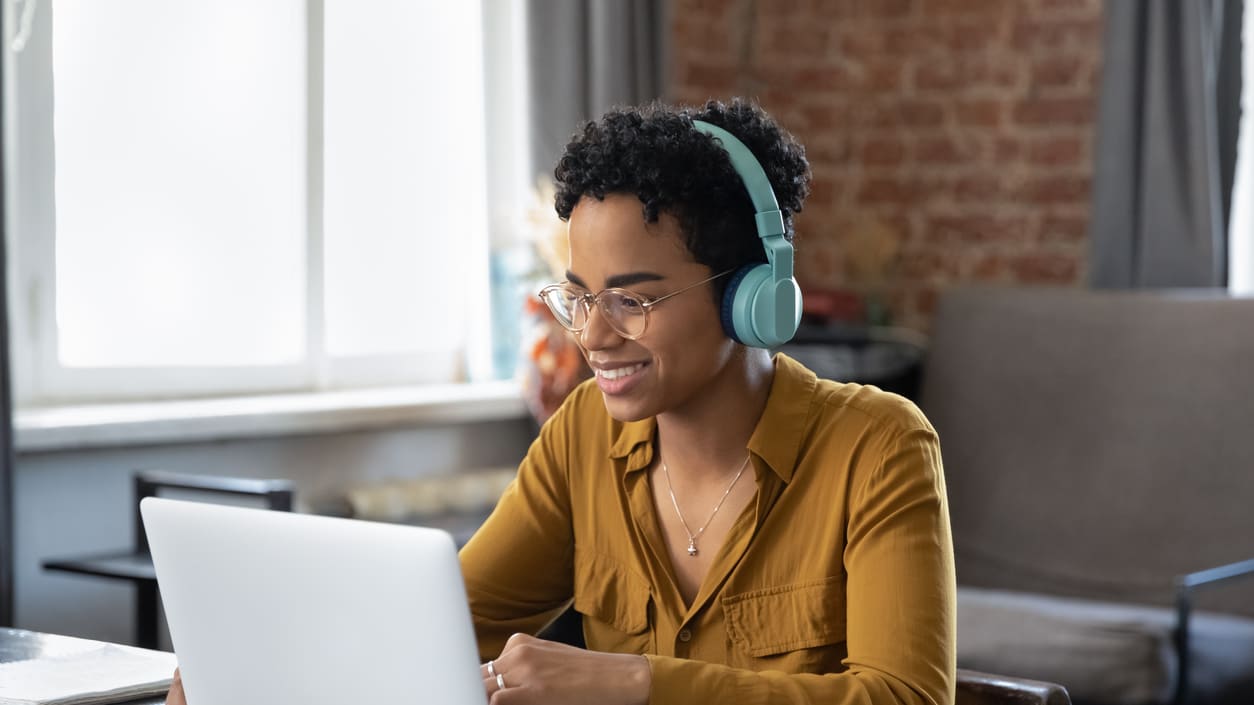 A woman wearing headphones is using a laptop at home.