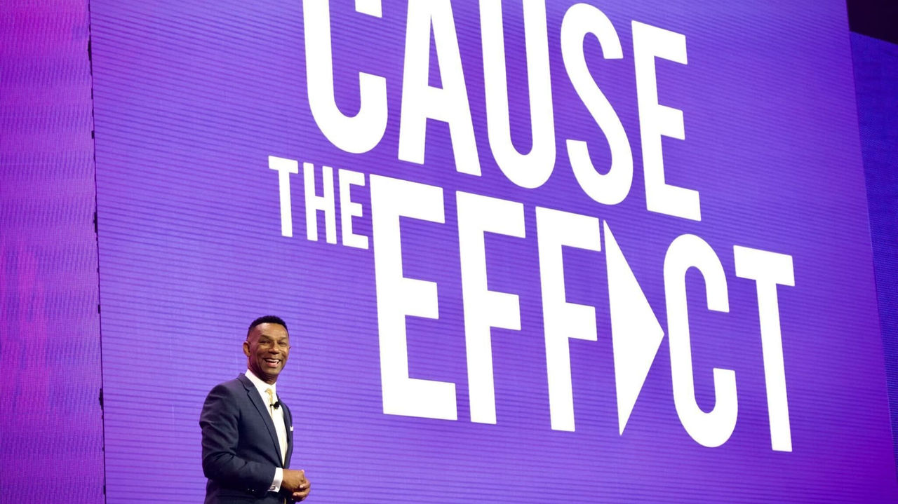 A man standing in front of a purple sign that says cause the effect.