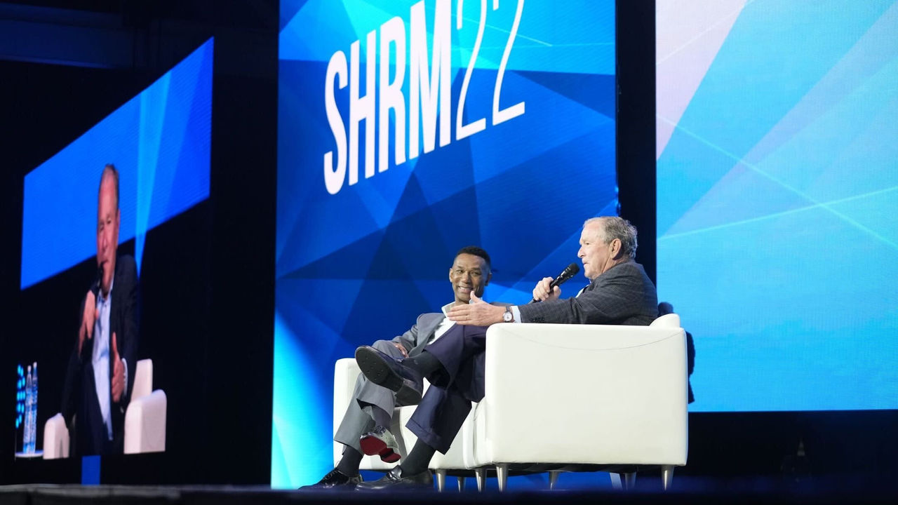 Two men sitting in chairs on stage at a conference.