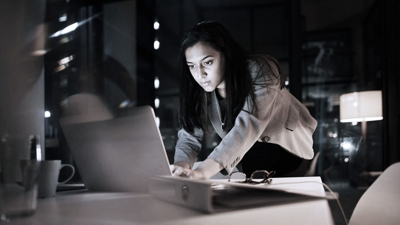 A woman working on a laptop in a dark room.