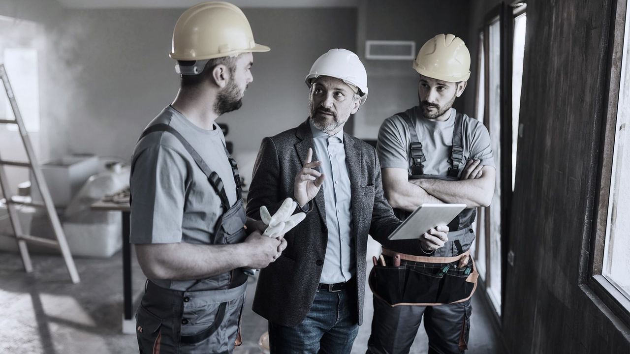 Three construction workers in hard hats talking to each other.