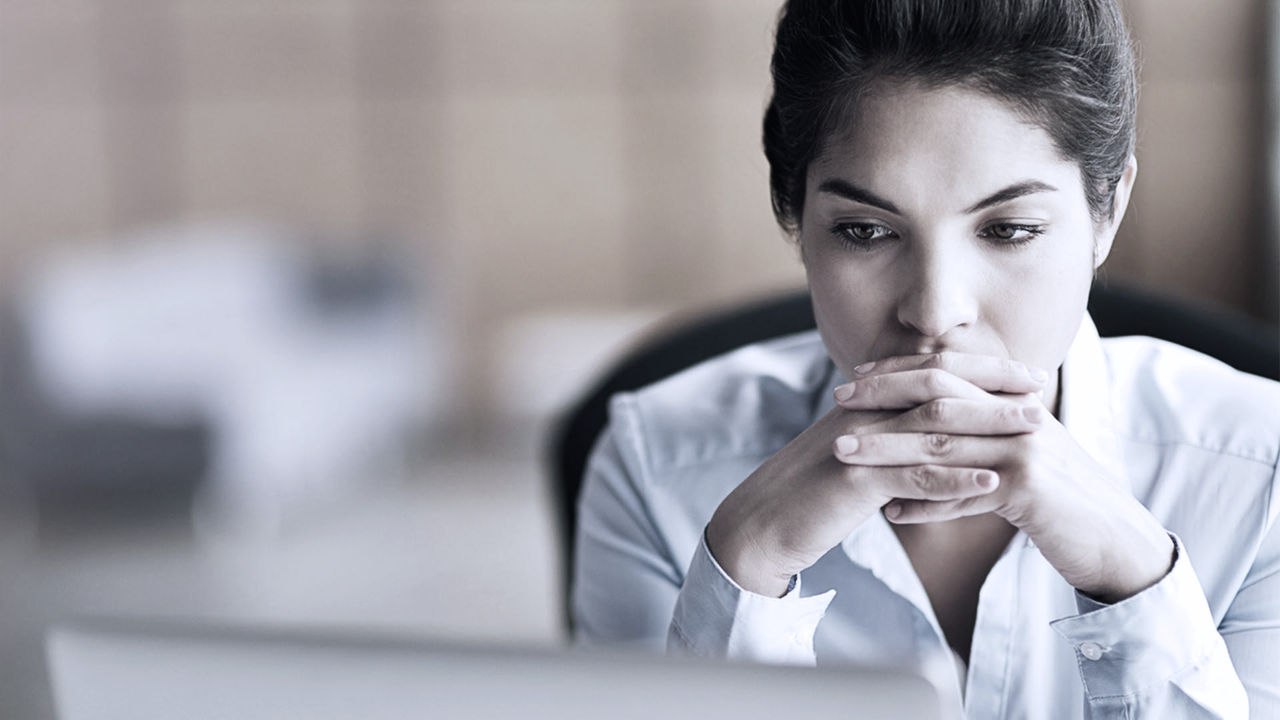 A woman is sitting in front of a laptop with her hand on her chin.