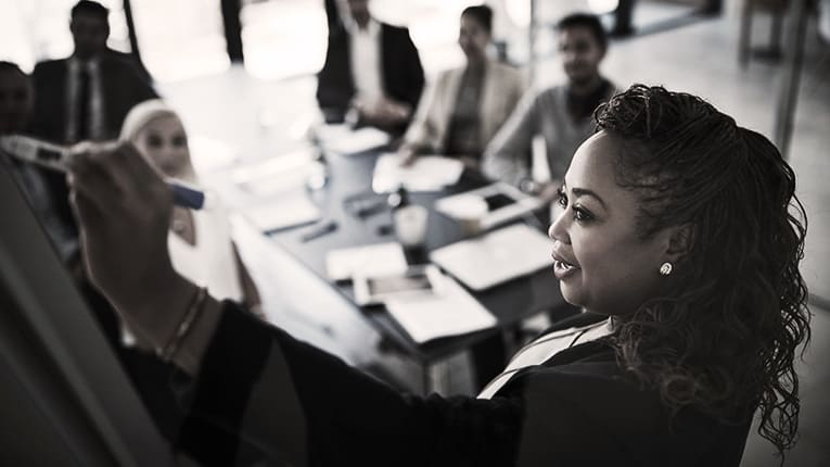 A woman in a business suit is writing on a whiteboard.