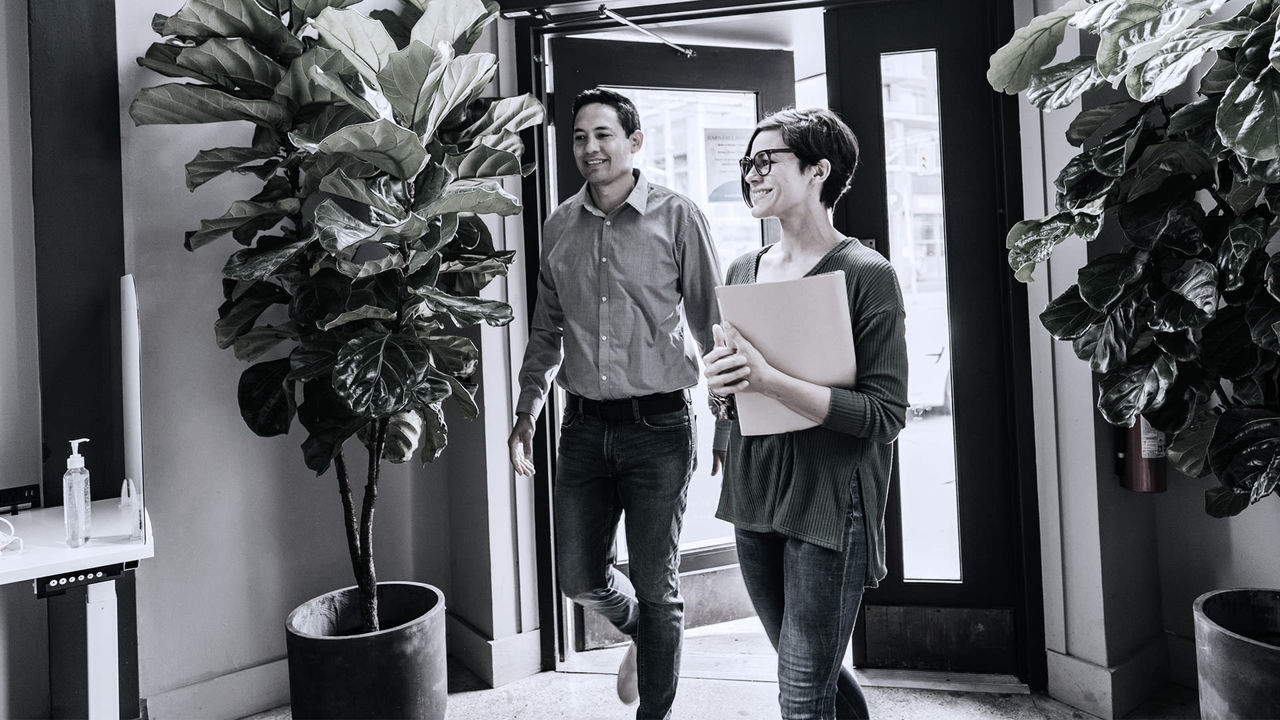 Black and white photo of a man and woman walking into an office.
