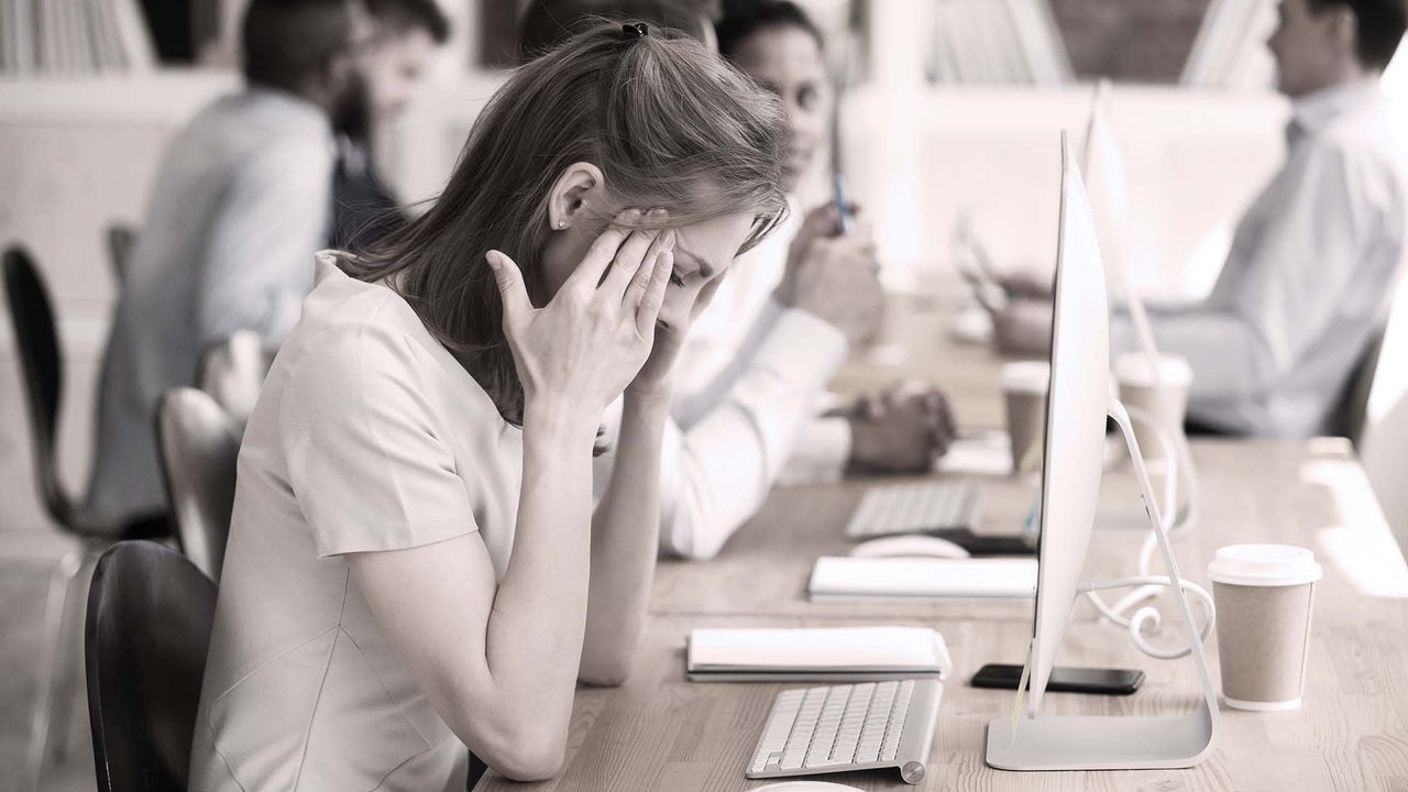 A woman is sitting at a desk with her hands on her face.