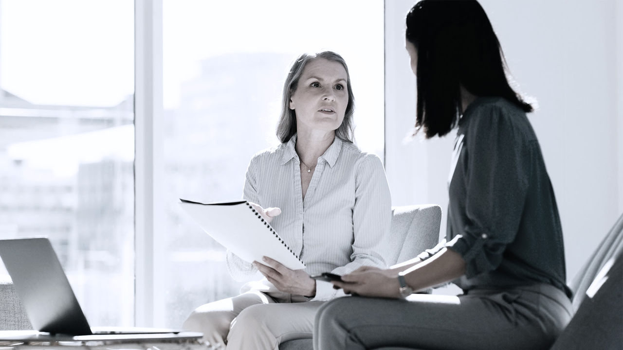 Two women sitting on a couch talking to each other.