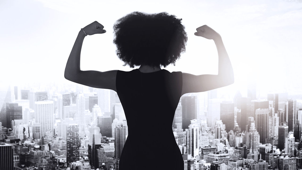 A silhouette of a woman flexing her muscles in front of a city.