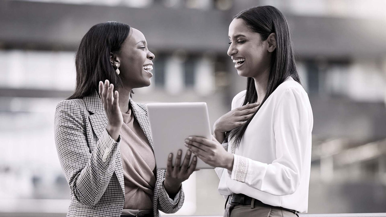 Two business women talking to each other on a tablet.