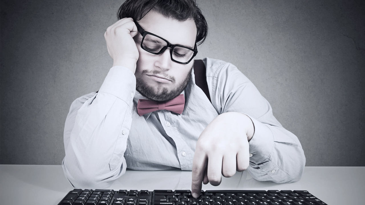 A man with glasses and a bow tie sitting on a keyboard.