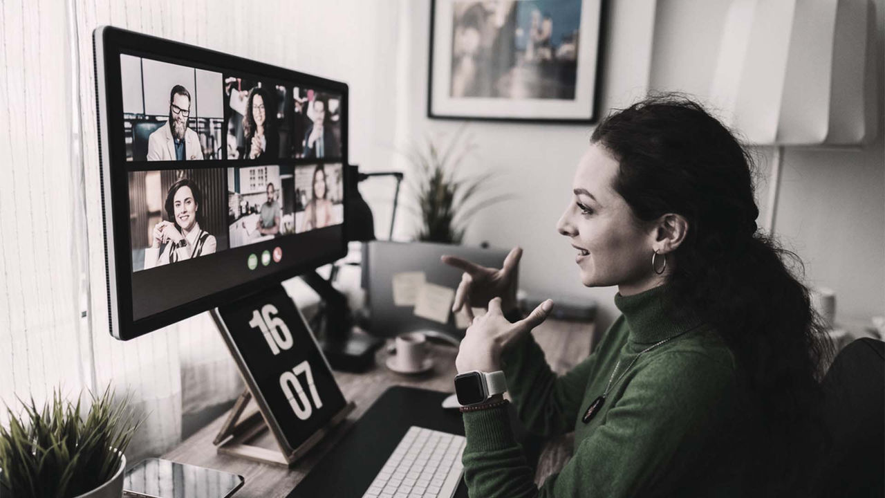 A woman is sitting in front of a computer with several people on the screen.