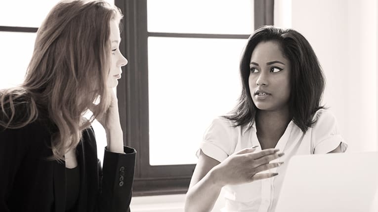 Two women talking in front of a laptop.