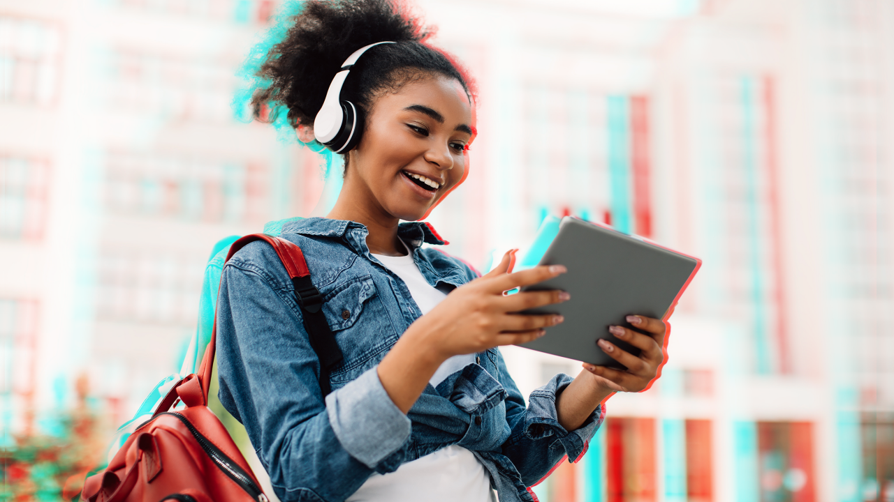 Vibrant young student with headphones on looking at tablet device outside in the city 