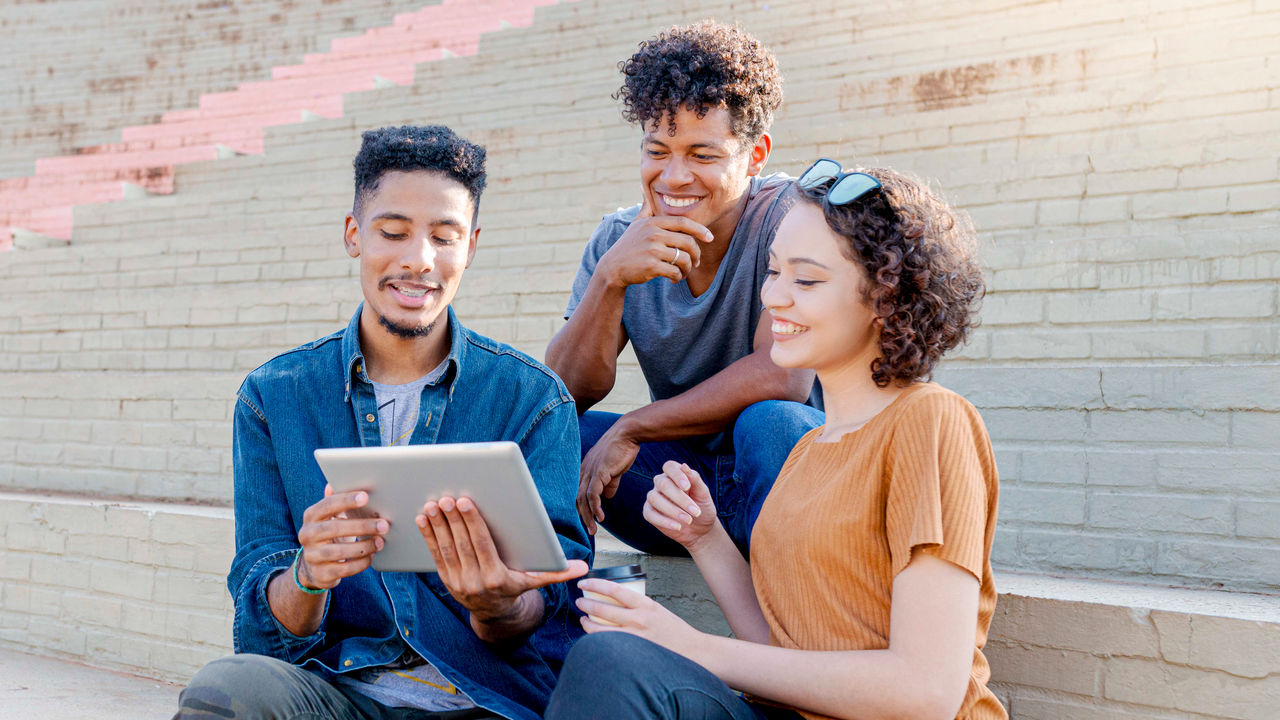 Three young people sitting on steps looking at a tablet computer.