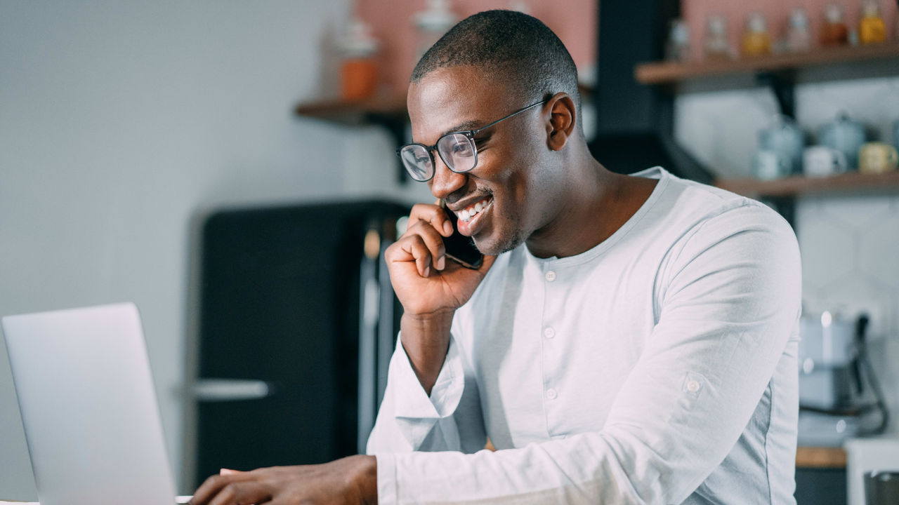 A man is talking on the phone while working on a laptop at home.