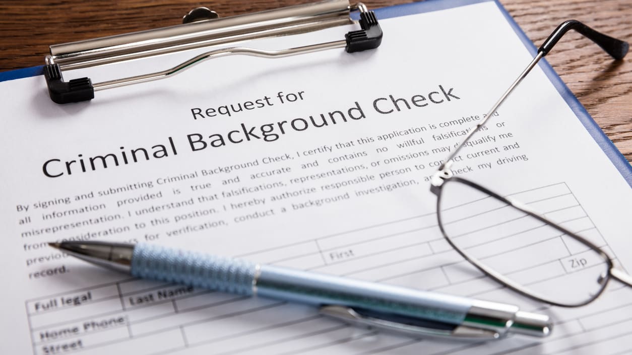 A criminal background check form with a pen and glasses on it on a clipboard on a desk.