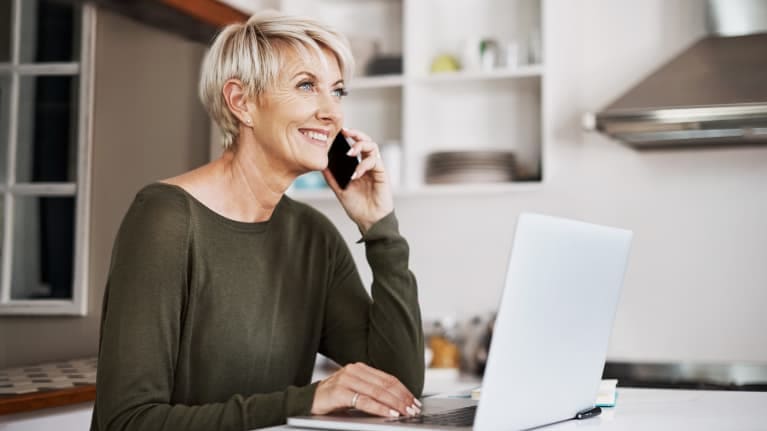 A woman is talking on the phone while sitting at her kitchen table.