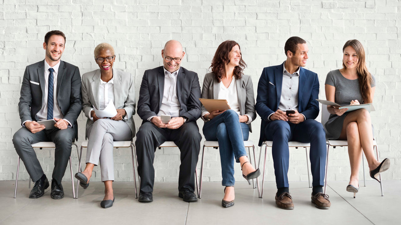 A group of business people sitting on chairs in front of a brick wall.