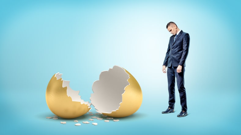 A businessman is standing next to an egg that has been broken.
