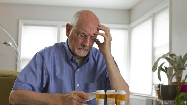A man sitting at a table looking at his pills.