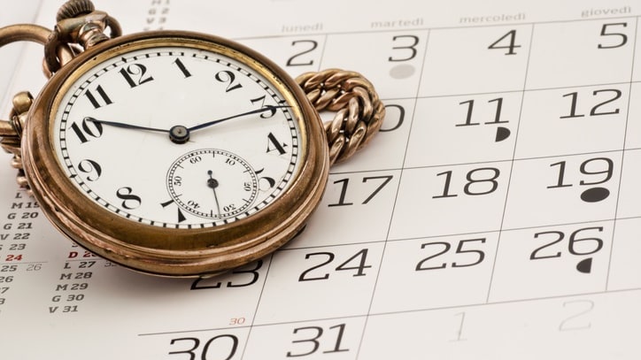 A pocket watch sits on top of a calendar.