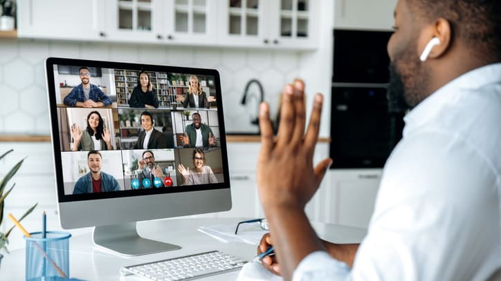 A man in front of a computer with a group of people on a video conference.