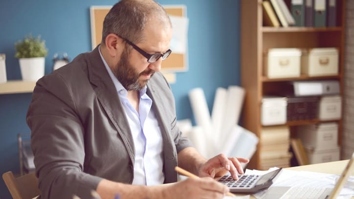 A man in a suit is using a calculator at his desk.