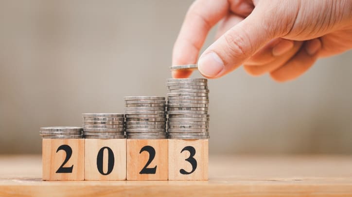 A hand putting coins into a stack of wooden blocks with the word 2023.