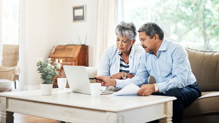 An older couple looking at documents on a laptop in their living room.