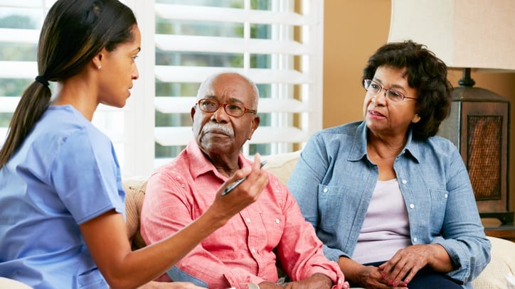 A nurse is talking to an older man and woman in a living room.