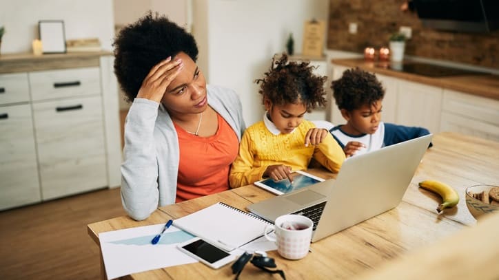 A woman and her children are working on a laptop at the kitchen table.