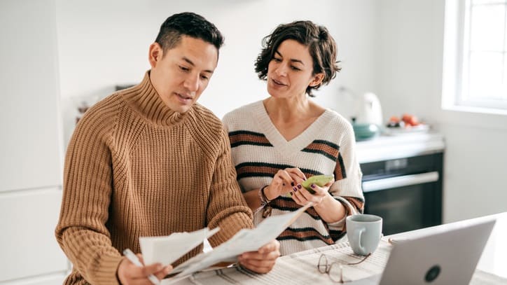 A man and woman are looking at a laptop at the kitchen table.