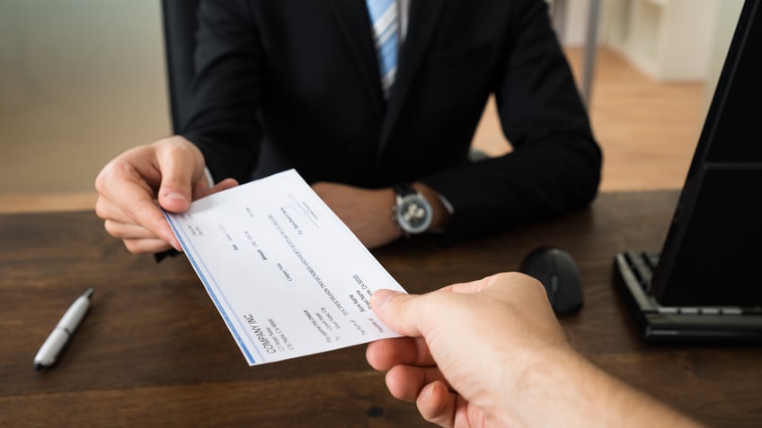 A businessman handing a check to another person in an office.