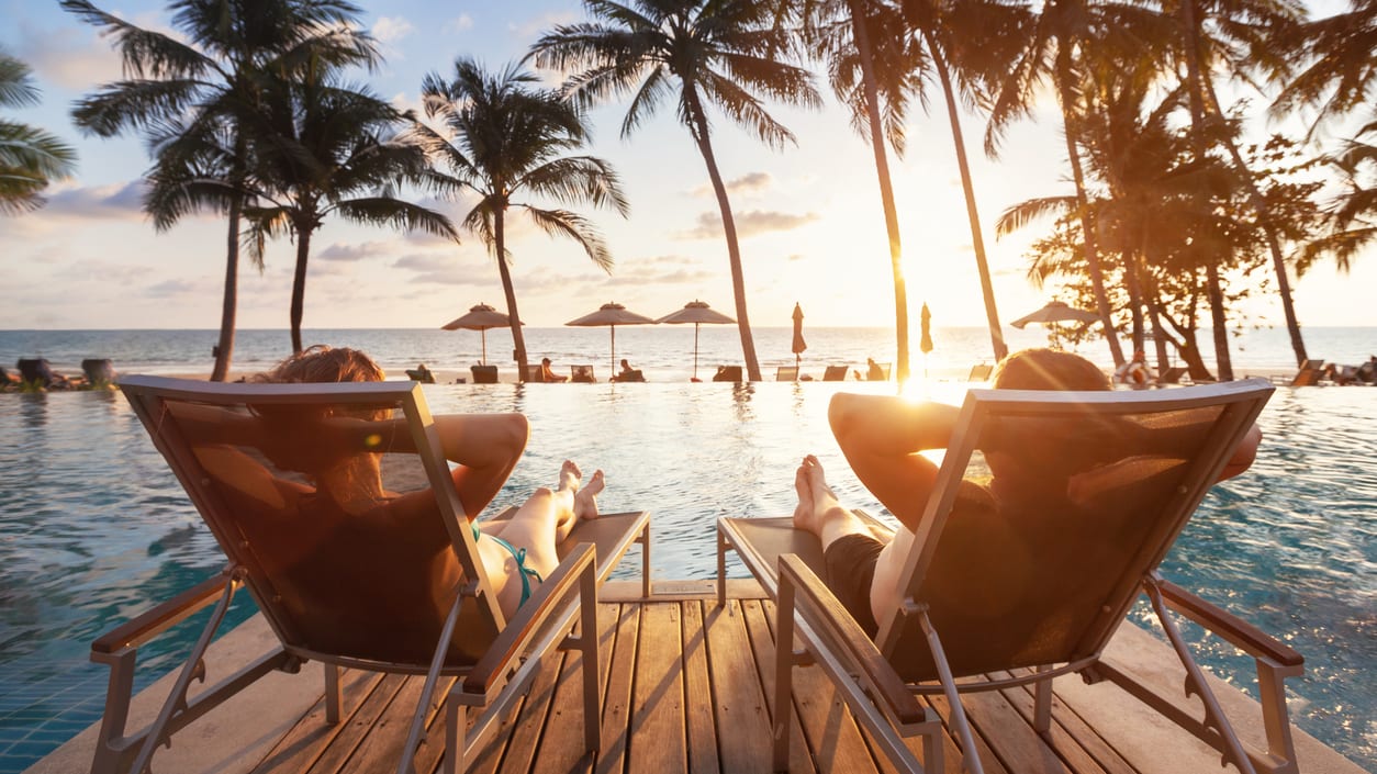 Two people relaxing in lounge chairs by the pool at sunset.