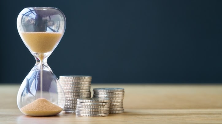 A sand hourglass sits next to a stack of coins.