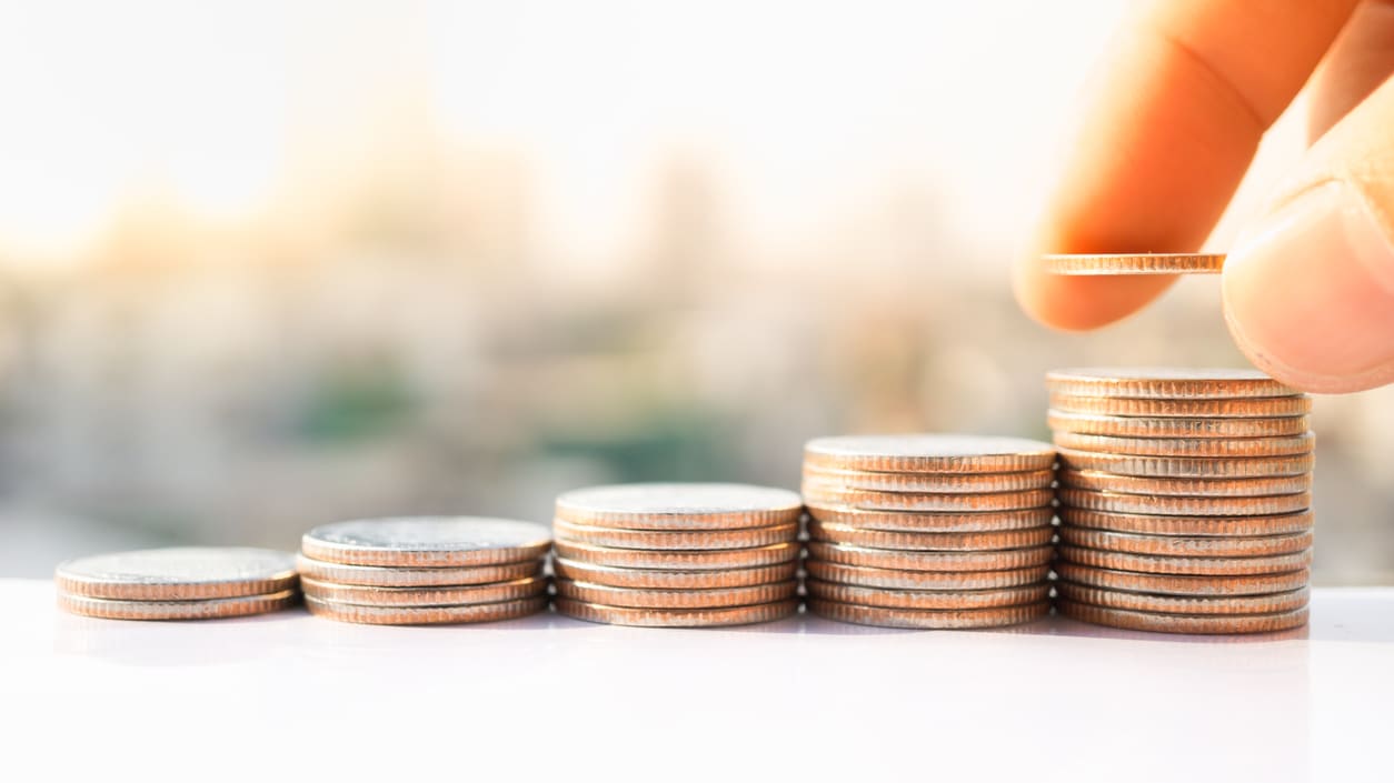 A hand is putting coins on top of a stack of coins.