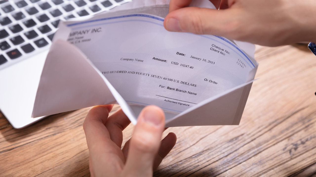 A man is holding a check in front of a laptop.