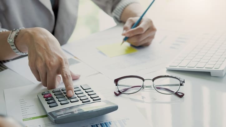 A woman is using a calculator at a desk.