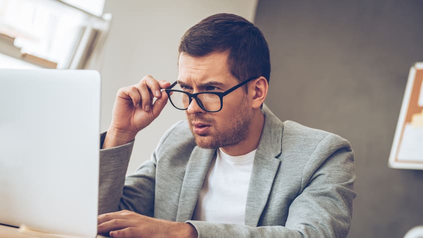 A man wearing glasses is working on his laptop.