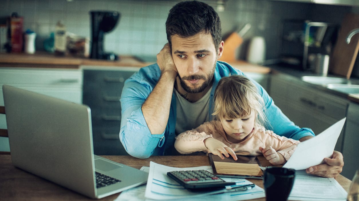 A man and a child sitting at a table with papers and a laptop.