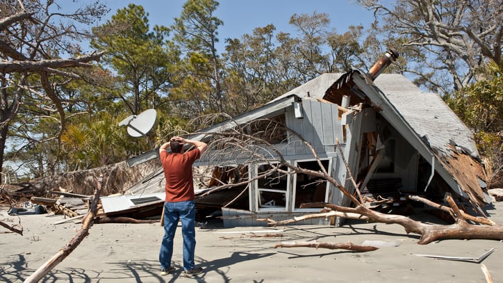 A man standing in front of a house that has been destroyed by hurricane katrina.