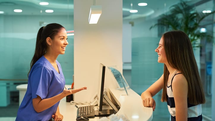 Two women talking at a reception desk in a dental office.