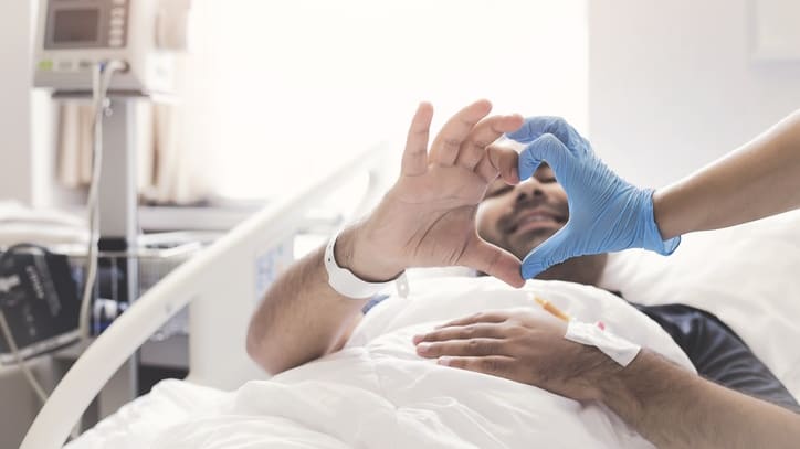 A man laying in a hospital bed with a blue glove on his hand.