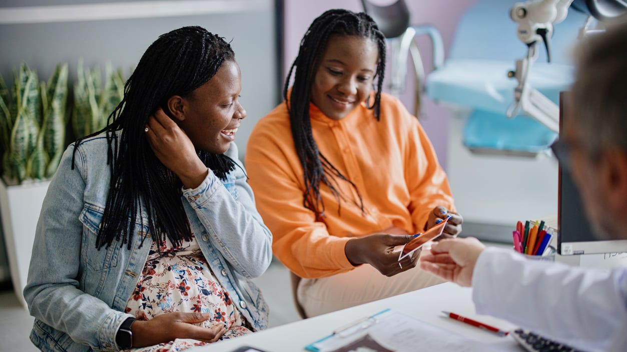 Two women sitting at a desk talking to a doctor.