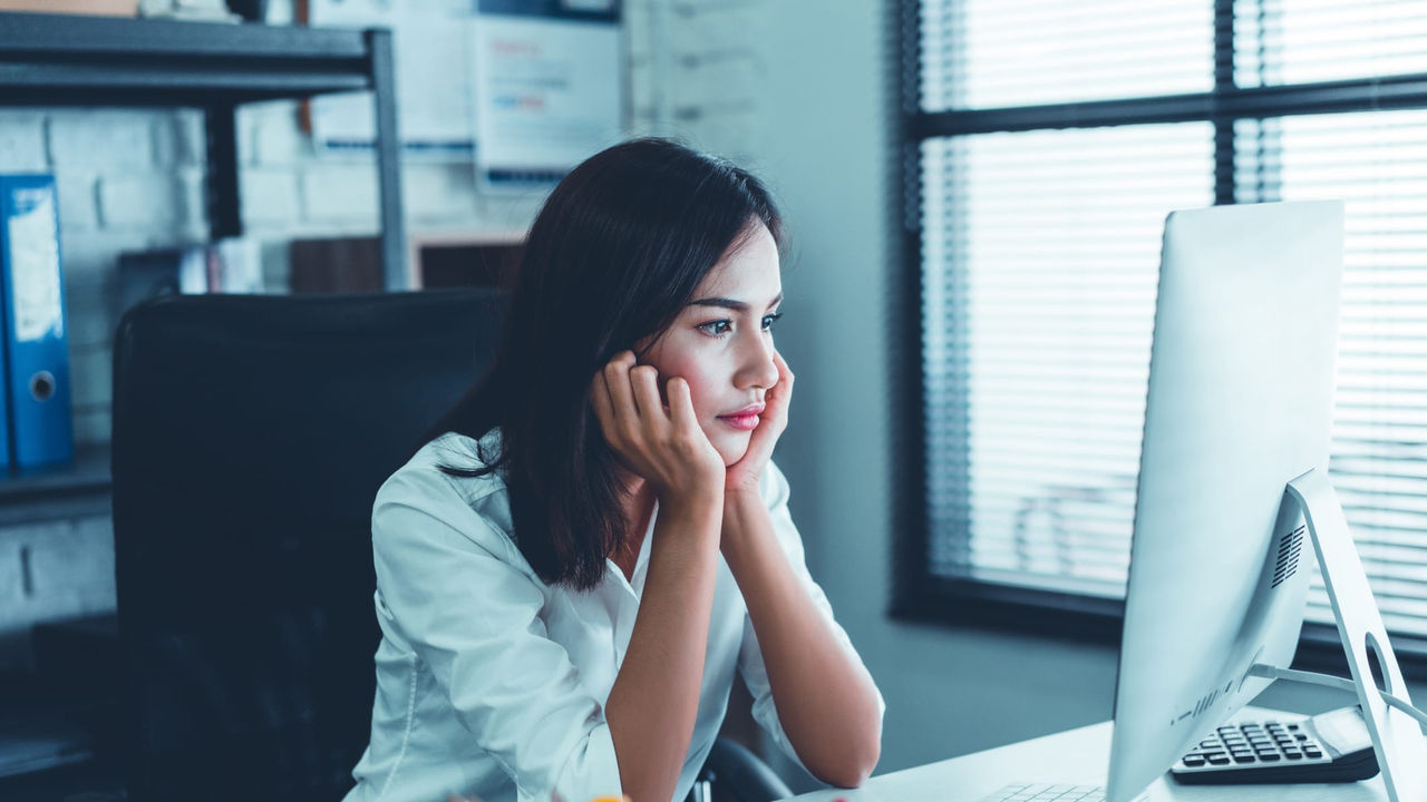 A woman sitting in front of a computer with her hand on her face.